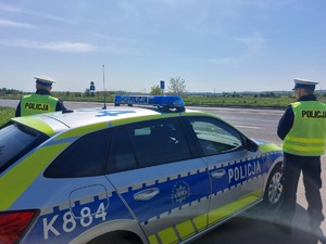 Policjanci stojący przy drodze tyłem, obok radiowozu