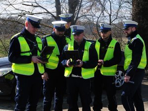 Na zdjęciu widocznych jest sześciu funkcjonariuszy, którzy spoglądają na kontrolery drona