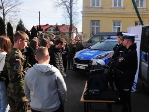 Na zdjęciu widoczna jest grupa młodzieży oraz policjanci na tle radiowozów