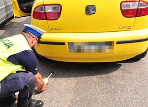 Policjant kucający przy końcówce wydechu kontrolowanego pojazdu i dokonujący pomiaru hałasu