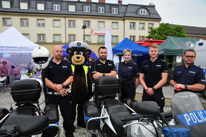 Czterech policjantów, policjantka oraz miś pozujący do zdjęcia przy policyjnych motocyklach