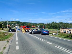 Zdjęcie przedstawia miejsce kolizji. Z prawej strony znajduję się seat oraz ford. W środkowej części wóz strażacki oraz strażacy, za nimi radiowóz. Z lewej strony uszkodzone mini.