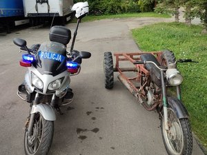 Policyjny motocykl. Obok zatrzymany do kontroli trójkołowiec.