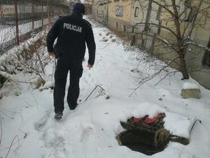 Policjant idący po śniegu wzdłuż opuszczonego budynku i otwartego włazu do studzienki