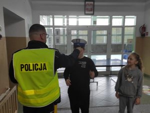 Policjant nakładający chłopcu na głowę białą czapkę policjanta ruchu drogowego