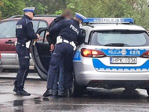 Policjanci wsadzający mężczyznę skutego w kajdankach do radiowozu