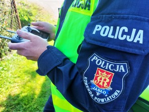 Ramię policjanta w kamizelce, którym trzyma w rękach pilota do drona