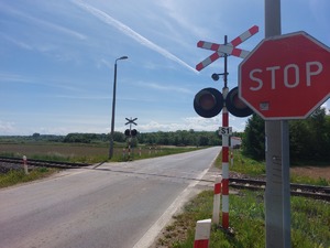 Znak stop, a za znakiem widoczny przejazd kolejowy wraz z krzyżem św. Andrzeja
