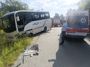 Z lewej autobus z widocznymi uszkodzeniami, który znajduję się częściowo w rowie. Z prawej karetka pogotowia