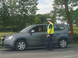 Policjant stojący przy aucie z żółtym alkomatem w ręku i rozmawiający z kierowcom