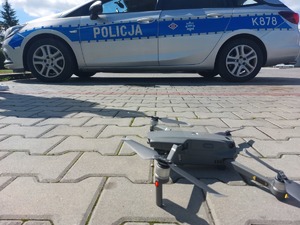 Dron na kostce brukowej, w tle radiowóz