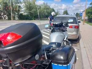 Policyjny motocykl, przed nim zatrzymany do kontroli samochód oraz stojący obok policjant