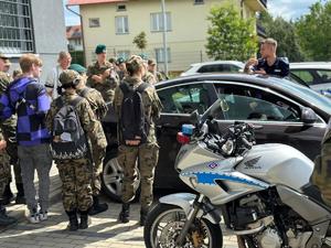 Na pierwszym planie motocykl, w tle uczniowie i nieoznakowany radiowóz