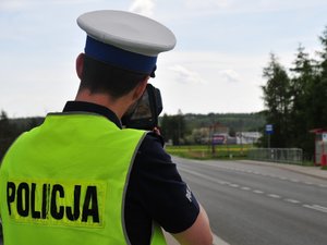 Policjant ruchu drogowego stojący przy jezdni i mierzący prędkość pojazdów