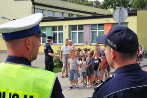 Policjant ruchu drogowego oraz dzielnicowy, w tle policjantka i dzieci