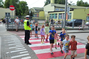 Policjant stojący przed przejściem dla dzieci, po którym dzieci idą w parach