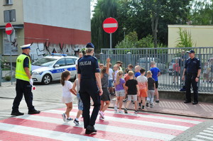 Policjanci stojący przed przejściem dla dzieci, po którym dzieci idą w parach