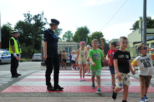 Policjanci stojący przed przejściem dla dzieci, po którym dzieci idą w parach