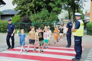 Policjanci stojący przed przejściem dla dzieci, po którym dzieci idą w parach