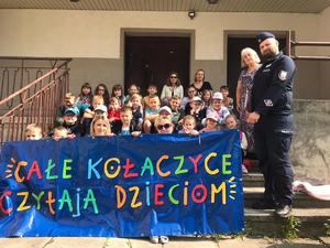 Dzieci trzymający baner z hasłem o czytaniu, obok nich dzielnicowy