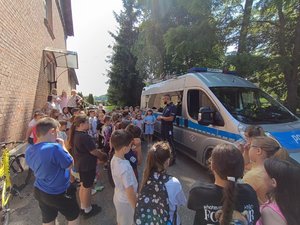 na zdjęciu widać policjanta stojącego przed radiowozem -prowadzącego pogadankę dla dzieci