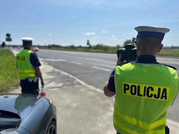 dwóch policjantów stoi na poboczu jezdni podczas wykonywania pomiaru prędkości