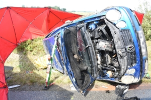 Uszkodzony i wywrócony na bok volkswagen. Obok czerwony parawan strażacki