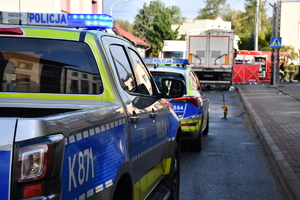 Radiowozy oraz wóz strażacki i namiot strażacki w tle