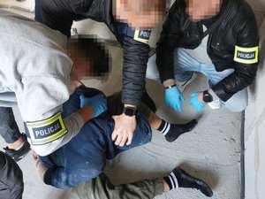 Zatrzymany mężczyzna siedzący na ziemi, obok funkcjonariusze kryminalni