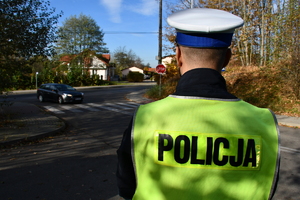 Policjant stojący tyłem przy wjeździe do cmentarza