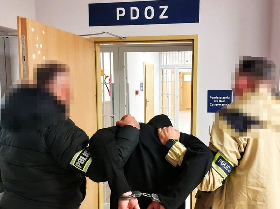 Policjanci kryminalni trzymający mężczyznę w kajdankach przed policyjną izbą zatrzymań
