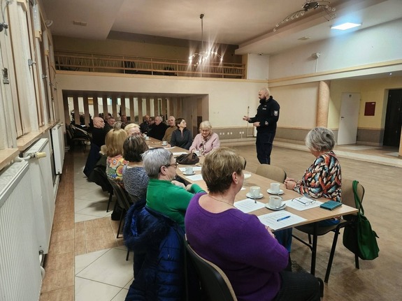 Na zdjęciu widzimy dzielnicowego, który mówi do zebranych seniorów